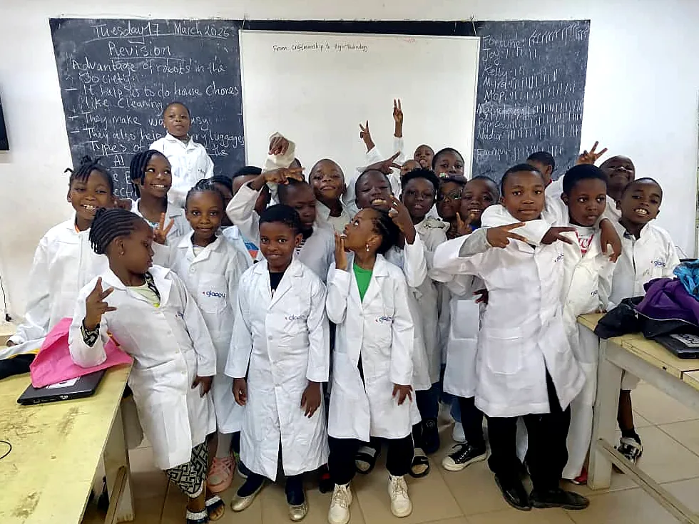 A big class in white lab coats cheers and waves in front of the chalkboard