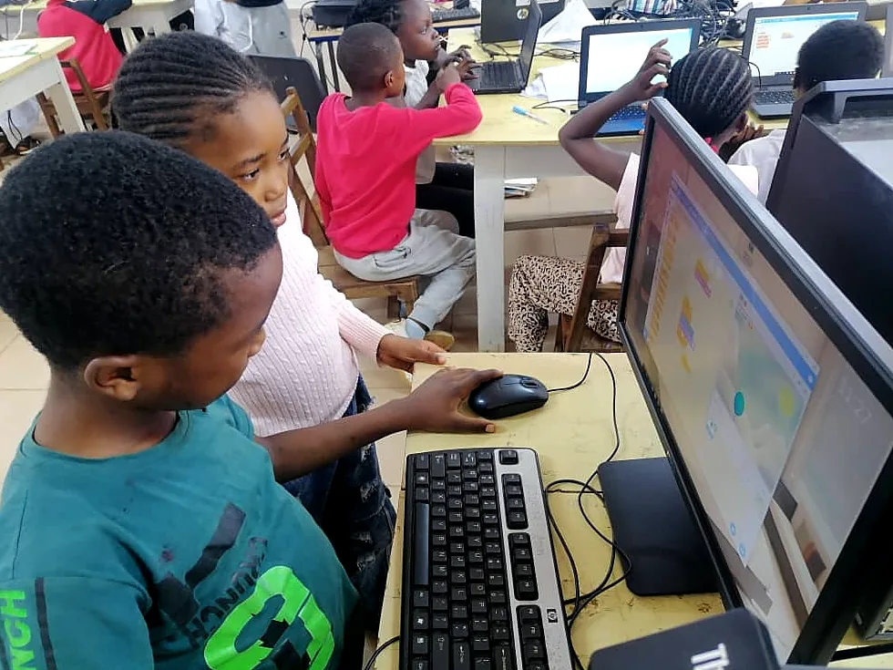 A boy in a green shirt concentrates on a coding exercise at a desktop computer