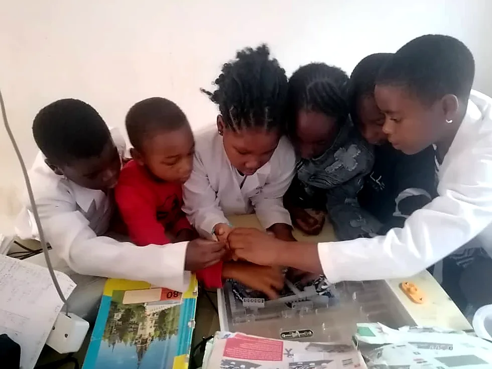 A small group of kids huddles close, hands on the same electronics project