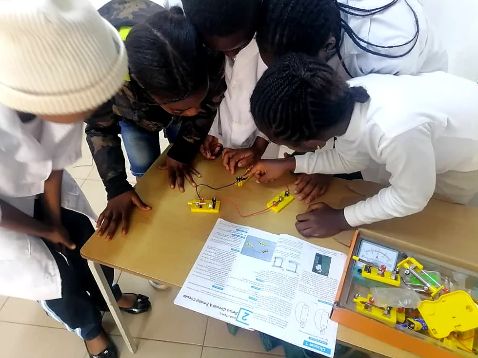 Children crowd around a desk, snapping together robotics parts beside an instruction sheet