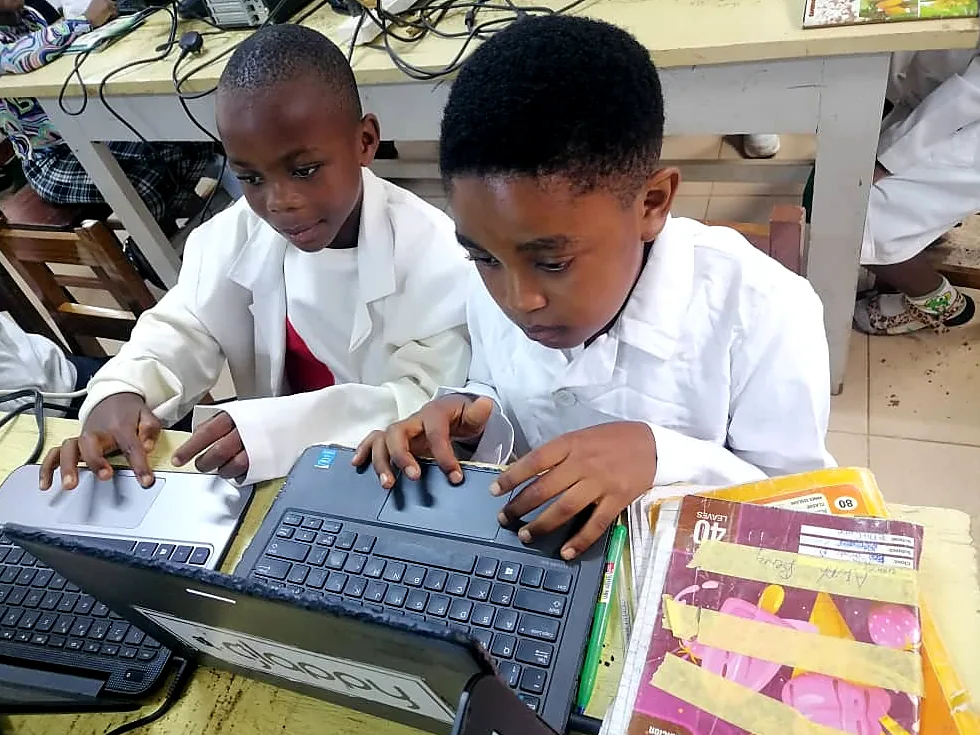 Two boys in lab coats type side by side on laptop keyboards in the classroom